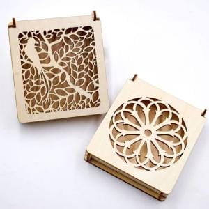 Zwei lasergravierte Holzkisten; eine mit einem Vogel und Blättern, die andere mit einem Blumenmuster. DIY-Geschenkboxen.