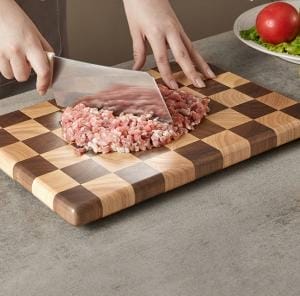 Person, die Hackfleisch auf einem dicken, karierten Walnuss-Schneidebrett hackt.