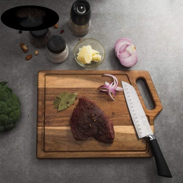 Schneidebrett aus Akazienholz mit Steak, roten Zwiebeln und Messer.
