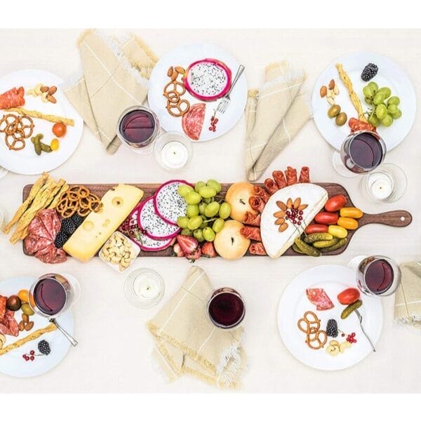 Wurstbrett mit Käse, Obst und Wein auf einem weißen Tisch. Käseplatte aus Walnussholz mit Griff.