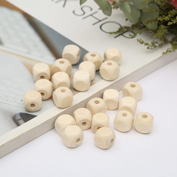 Naturfarbene, eckige Holzperlen mit großem Loch auf einem Buch. Polygonale Perlen für Großhandel.