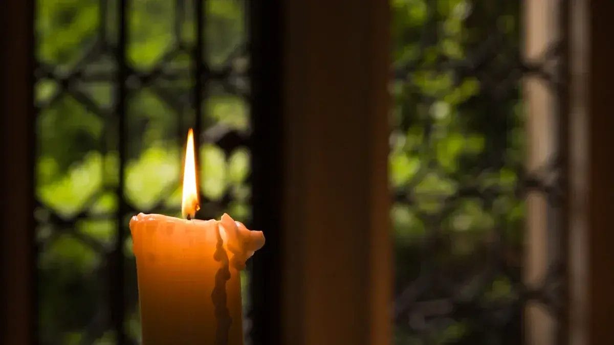 Brennende Kerze in einem Kerzenhalter vor einem Fenster. Anleitung zum Kerzen fixieren.