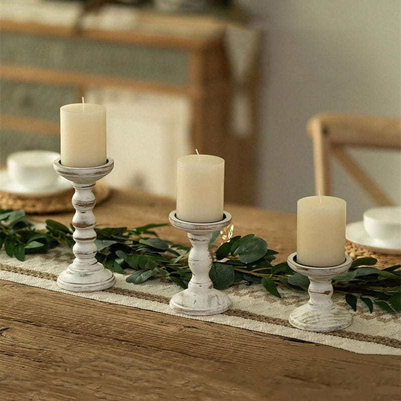 Rustikale Holzkerzenständer mit weißen Kerzen auf einem Tischläufer.