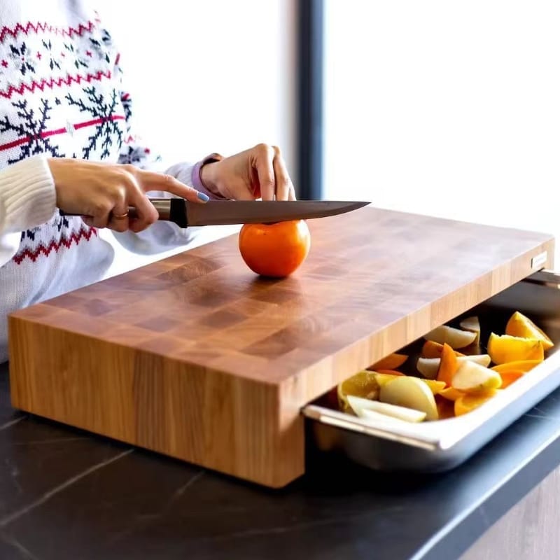 Frau schneidet Persimone auf Schneidebrett mit Schublade. Holz Schneidebrett mit Auffangschale sichtbar.