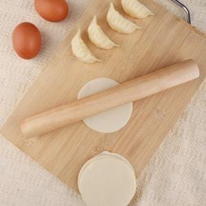 Holz Teigroller auf Schneidebrett mit Teig, Eiern und Teigtaschen.