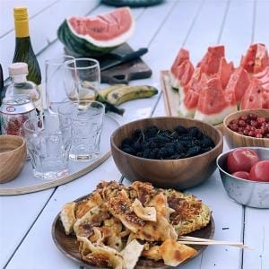 Holz Dekotablett mit Sommerfrüchten, Melone, Beeren und herzhaften Snacks auf einem Tisch.
