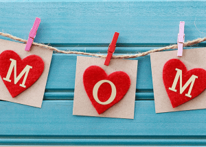 Holzherzen mit Buchstaben "MOM" auf blauem Hintergrund. Bastelidee.
