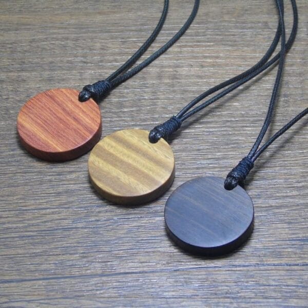 Personalisierbare Holzschmuck Anhänger in verschiedenen Farben auf Holzhintergrund.