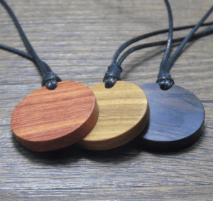 Personalisierbare Holzschmuck Anhänger in verschiedenen Farben auf Holztisch.