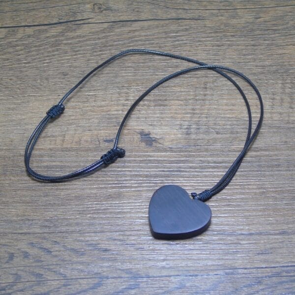 Herzförmiger Holzschmuck Anhänger an einer schwarzen Kordel auf Holzgrund.