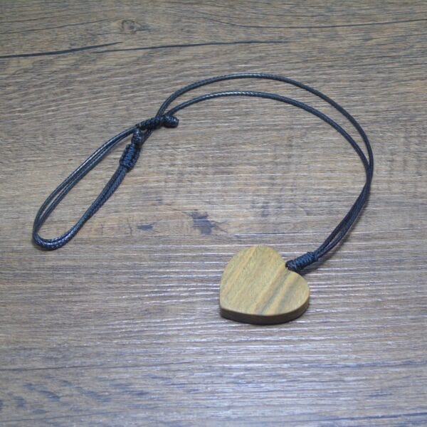 Herzförmiger Holzanhänger an schwarzer Kordel auf Holzgrund. Personalisierbarer Holzschmuck.