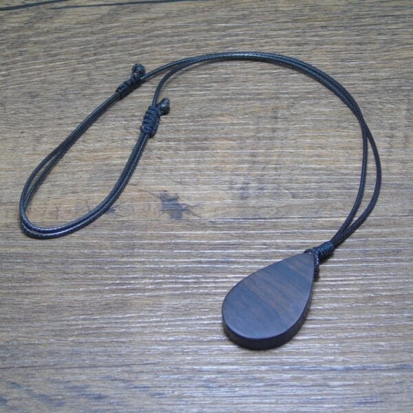 Dunkler, tropfenförmiger Holzanhänger an schwarzer Kordel. Personalisierbarer Holzschmuck.
