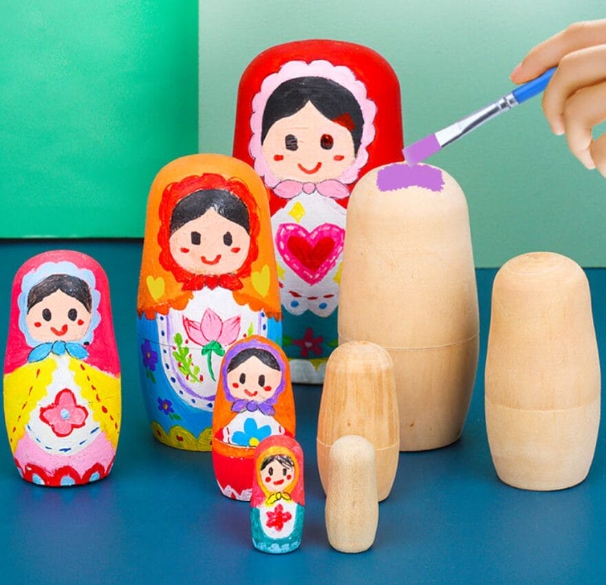 Bemalte Matroschkas und eine unbemalte, die mit lila Farbe bemalt wird.