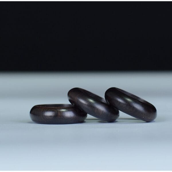 Drei dunkle Holzringe auf hellem Untergrund. Schlichte, elegante Schmuckstücke.