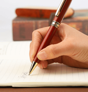 Hand schreibt mit einem edlen Holzkugelschreiber in ein Notizbuch. Personalisierte Kugelschreiber aus Holz.