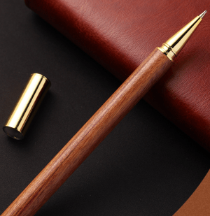 Wooden pen resting on a leather journal with a gold cap